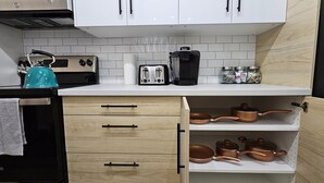 A kitchen with white cabinets, a kettle, a toaster, a coffee maker, and copper cookware on shelves.