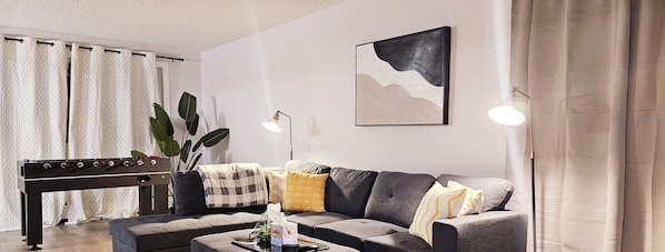 Un salon moderne avec un canapé, une table basse, un baby-foot et un grand tableau abstrait accroché au mur.