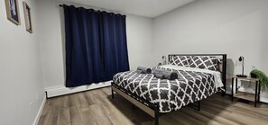Une chambre à coucher avec un lit, des rideaux foncés, une table de chevet avec une lampe et une petite plante en pot.