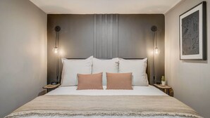 A neatly made bed with a headboard, two bedside lamps, and a framed artwork on the wall. - Blackstone Hideaway! Downtown Lower-Level Apt! (Colorado Springs)