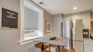 A modern kitchen with a marble countertop, two brown chairs, a stainless steel refrigerator, and a window with blinds. - Blackstone Hideaway! Downtown Lower-Level Apt! (Colorado Springs)