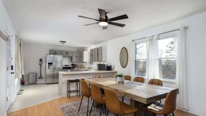 Una cocina moderna con una isla central, un comedor con mesa y sillas de madera, y un ventilador de techo.