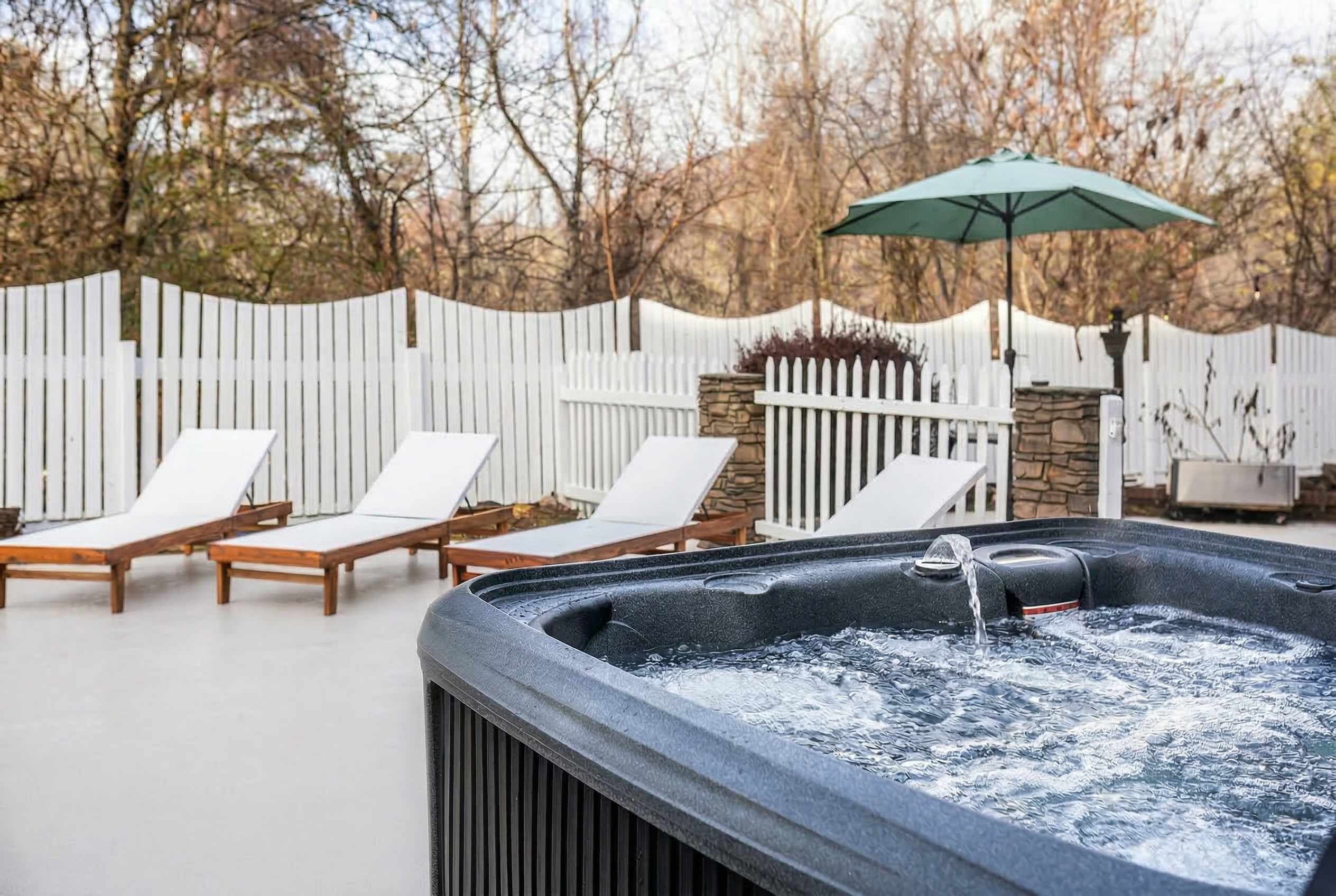 Un bain à remous rempli d’eau, entouré de chaises longues et délimité par une clôture blanche.