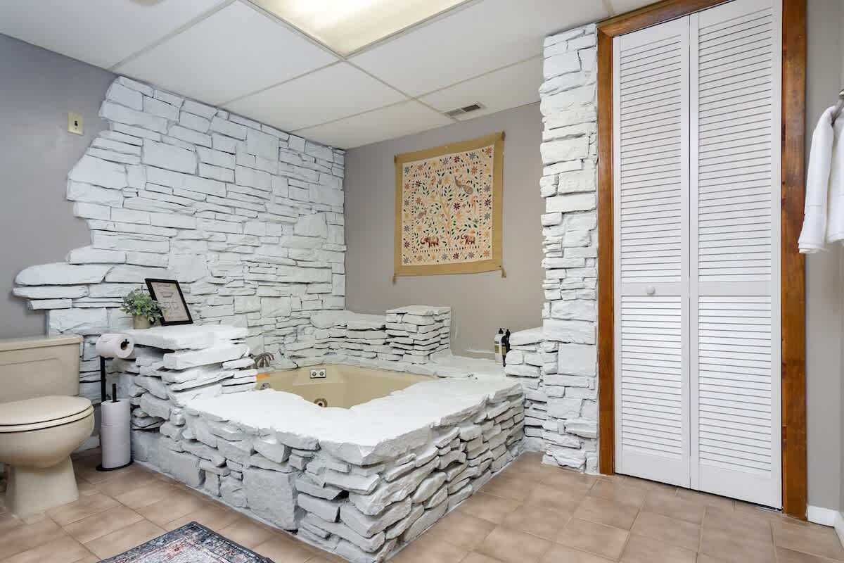 A bathroom with a stone wall, a bathtub, a toilet, and a shower area.