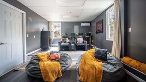 Un salón moderno con una paleta de colores gris y blanco, que incluye dos puffs, un sofá negro y un comedor con sillas.