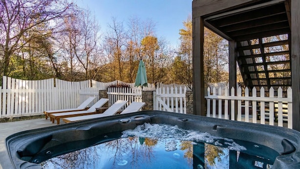 Un jacuzzi con un muelle de madera, cerca blanca y sillas de descanso.