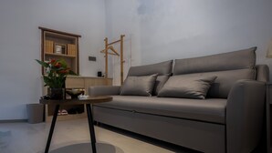 Una sala de estar moderna con un sofá gris, una mesita redonda pequeña y una estantería de madera.