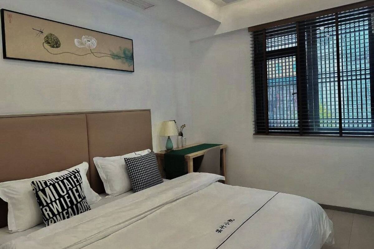 A hotel room with a bed, a nightstand, a lamp, and a window with blinds.