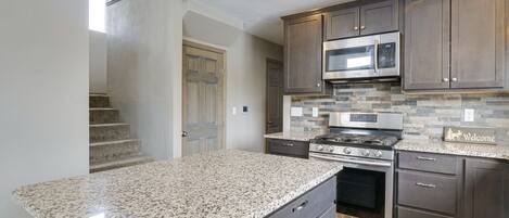 A kitchen with granite countertops, dark cabinetry, a stainless steel microwave, and a built-in oven.