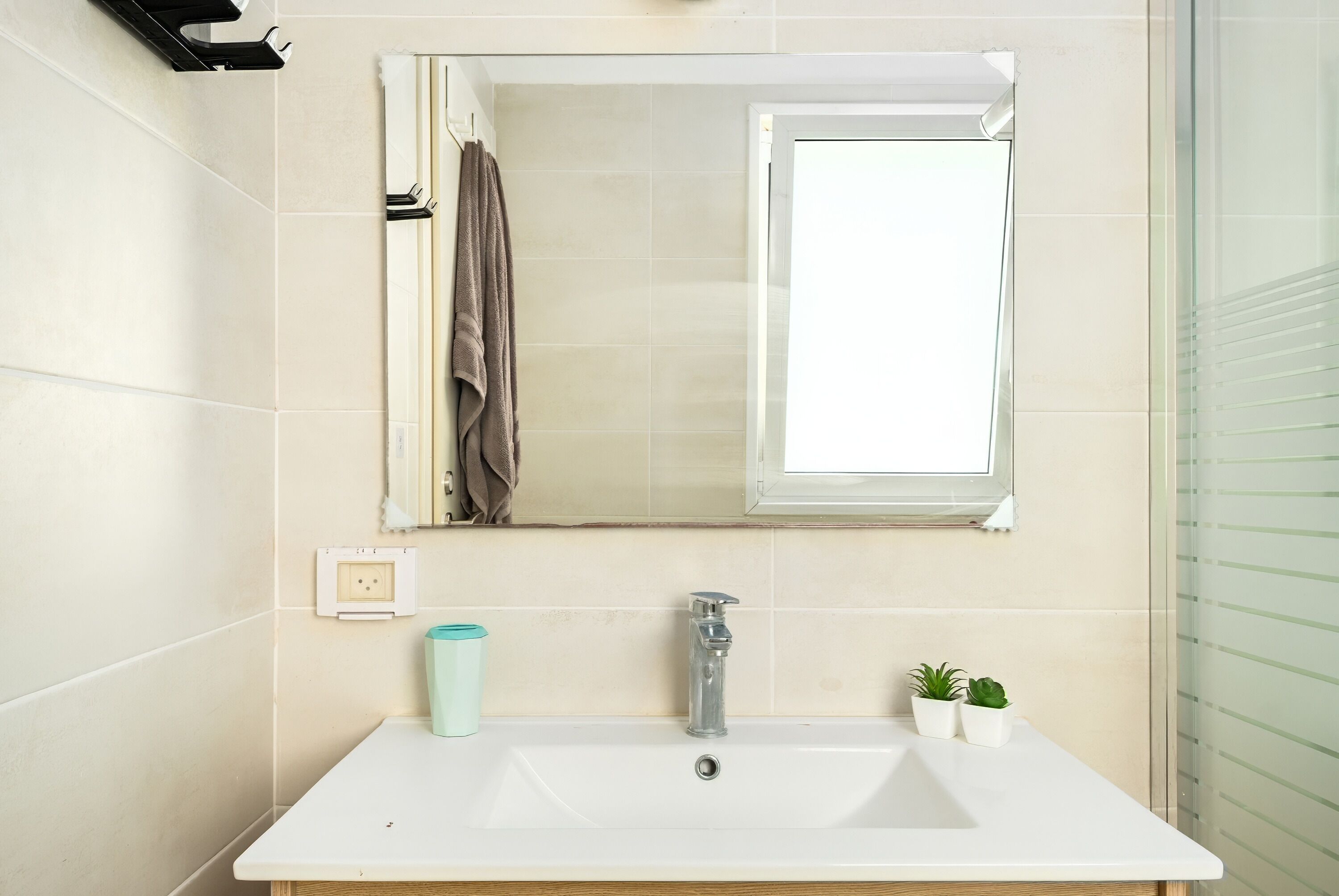 A bathroom with a white sink, a mirror, a towel rack, a window, and a small plant.