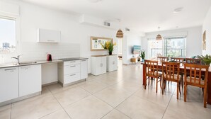 A modern kitchen with white cabinets, a dining area with wooden chairs, and a large window offering a city view. - MAMAD - Sea Breeze Netanya Retreat by Sea N Rent (Netanya)