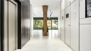 A modern hallway with a central wooden pillar, glass doors, and a view of greenery outside. - MAMAD - Sea Breeze Netanya Retreat by Sea N Rent (Netanya)