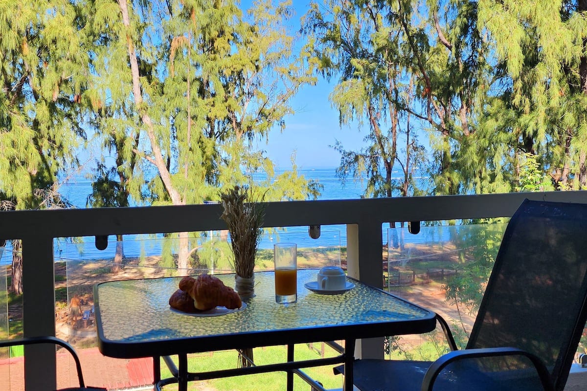 Un balcon avec une table, des chaises et une vue sur la mer et les arbres.