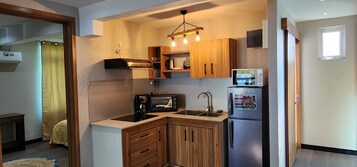 Cocina compacta con armarios de madera, microondas integrado, cafetera y refrigerador.