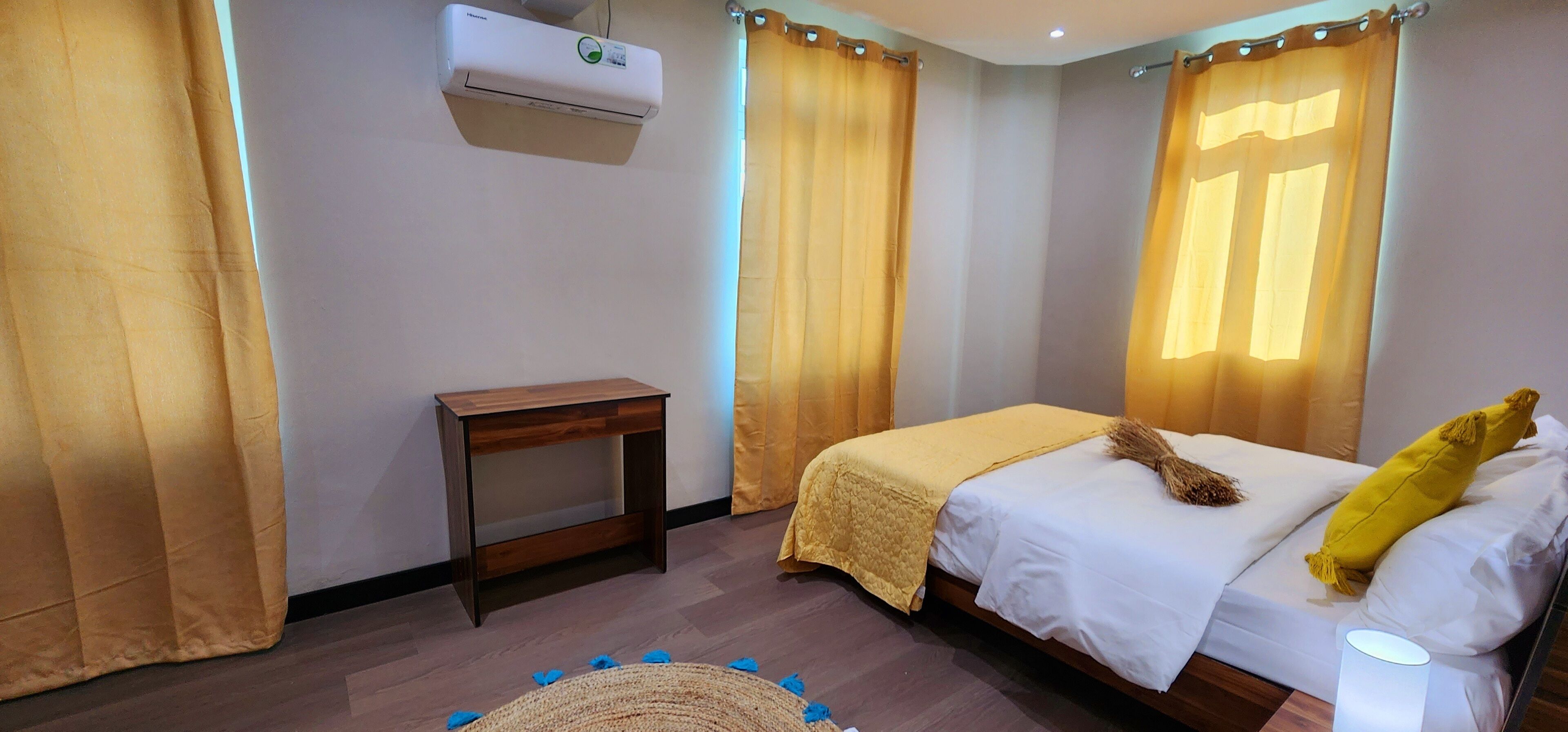 Une chambre à coucher comprenant un lit, une table de chevet, un climatiseur fixé au mur et des rideaux.