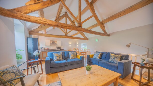 A spacious living area with a high ceiling and exposed wooden beams, furnished with sofas and a coffee table. - Unique barn conversion, sleeps up to 6 in 3 bedrooms, near to High Peak Trail. (Buxton)
