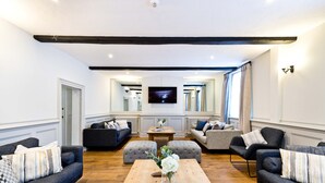 A modern living room with a wooden coffee table, two sofas, a television, and a large window. - The Crewe & Harpur pub, a unique exclusive self catering venue, sleeps up to 34. (Buxton)