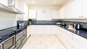 A modern kitchen with stainless steel appliances, white cabinets, a black countertop, and a clock on the wall. - The Crewe & Harpur pub, a unique exclusive self catering venue, sleeps up to 34. (Buxton)