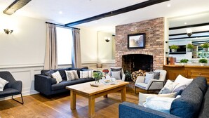 A living room with a brick fireplace, a wooden coffee table, and a sofa set. - The Crewe & Harpur pub, a unique exclusive self catering venue, sleeps up to 34. (Buxton)