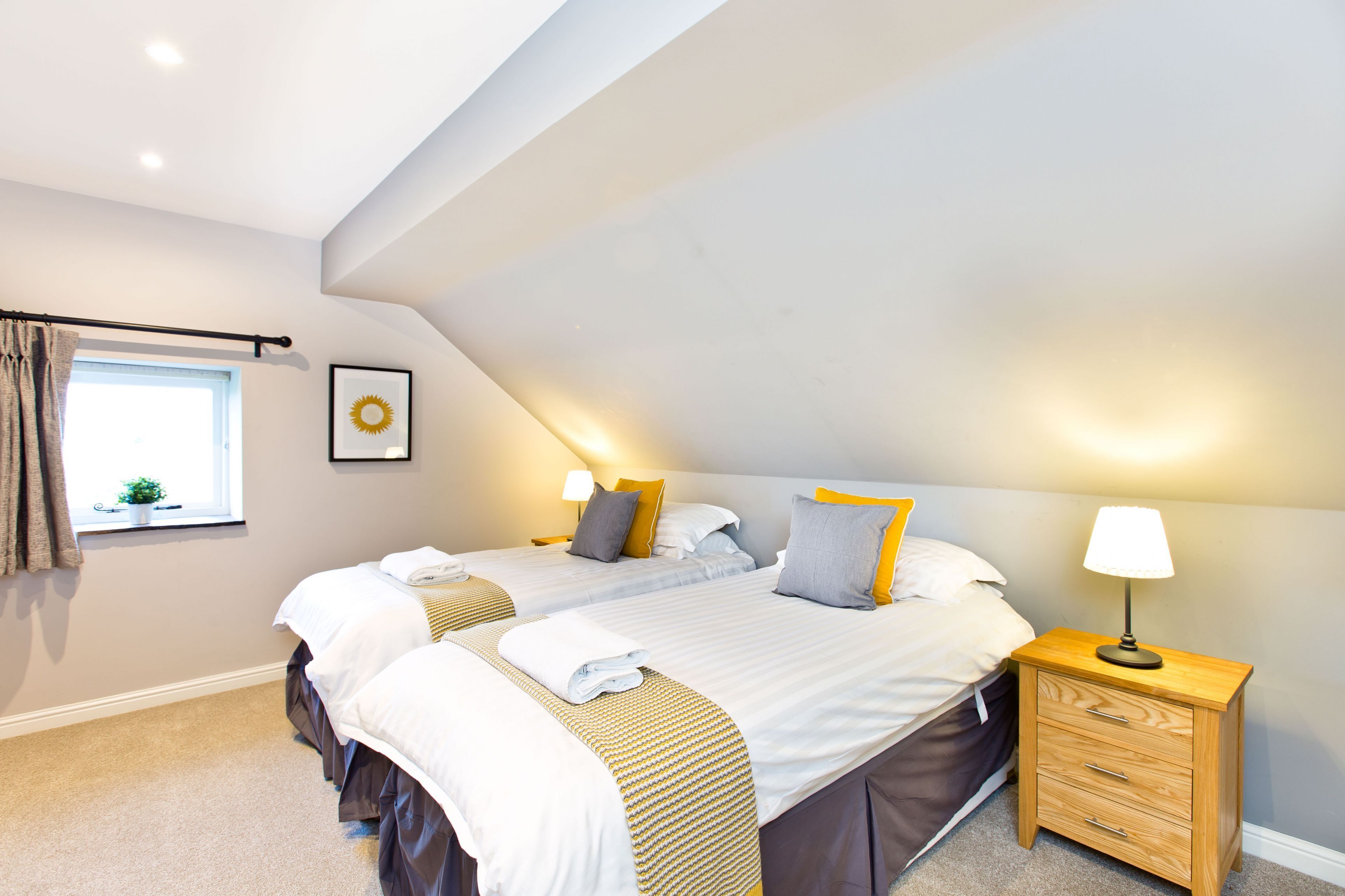 Une chambre avec deux lits, une fenêtre avec des rideaux, une table de chevet avec une lampe et une petite plante sur le rebord de la fenêtre.
