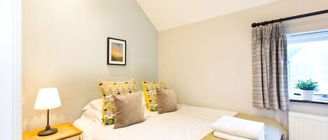 A neatly arranged bedroom with a bed, bedside table, lamp, and a window with curtains.