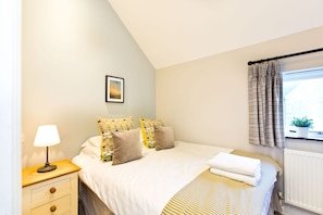 Quarto bem arrumado com cama, mesa de cabeceira, abajur e janela com cortinas.