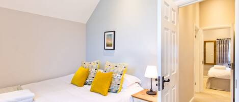 A bedroom with a bed, pillows, a bedside table, a lamp, and a door leading to a bathroom.
