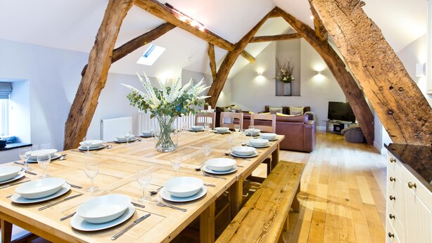 A dining area with a long wooden table set for a meal, a wooden bench, and a rustic ceiling structure. - Quirky barn conversion, sleeps 8 in 4 bedrooms, near to the High Peak Trail. (Buxton)