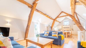 A spacious loft with exposed wooden beams, a blue sofa set, a wooden coffee table, and a television. - Quirky barn conversion, sleeps 8 in 4 bedrooms, near to the High Peak Trail. (Buxton)