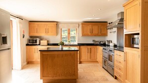 A modern kitchen with wooden cabinets, a central island, stainless steel appliances, and a window providing natural light. - Lapwing Barns, large rural farmhouse with games room, perfect for all types of groups. (Longnor)
