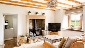 A cozy living room with a stone fireplace, a television, and a window with a view of the outdoors. - Lapwing Barns, large rural farmhouse with games room, perfect for all types of groups. (Longnor)