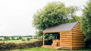 Une cabane en bois dotée d’un porche, entourée d’un mur de pierres et d’une végétation luxuriante.