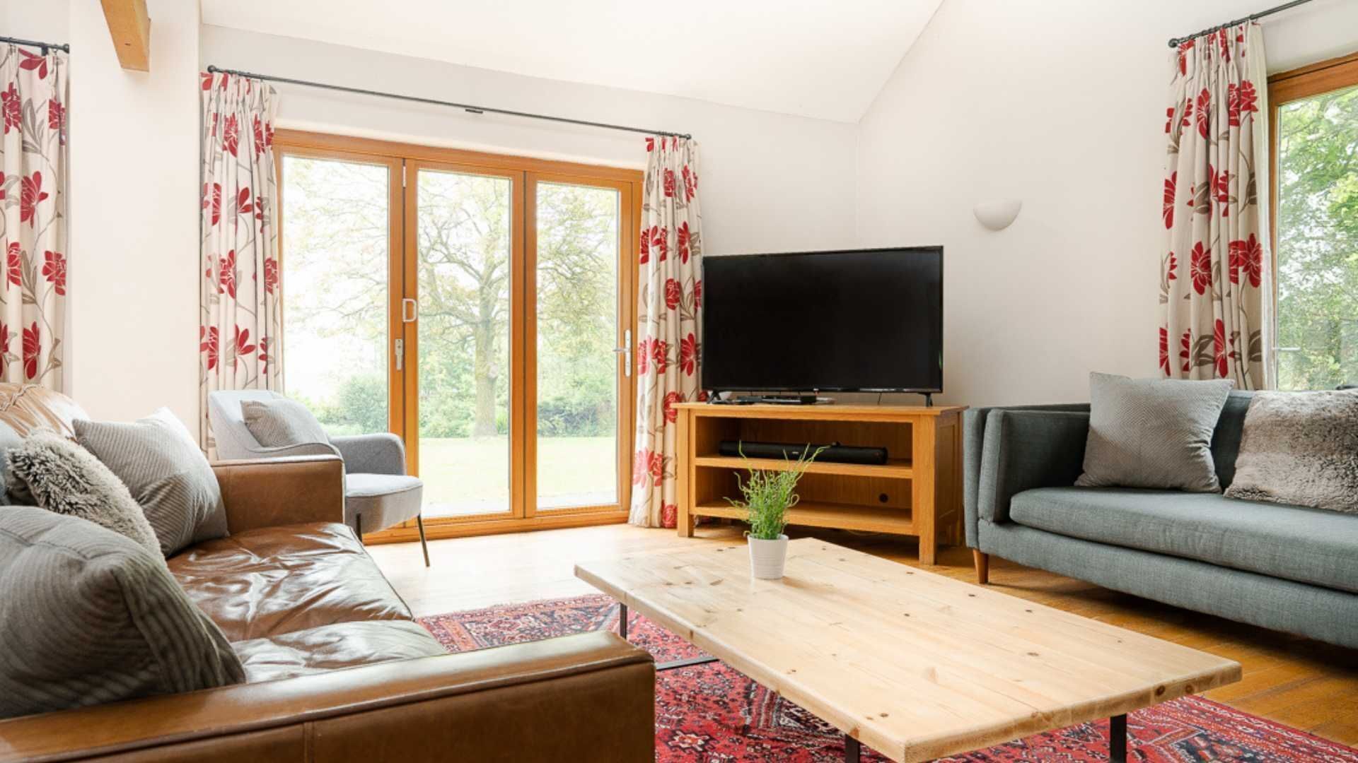 A living room with a leather sofa, a grey sofa, a wooden coffee table, and a TV on a wooden stand.
