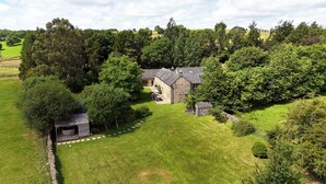 Une maison en pierre dotée d’un porche en pierre, entourée d’une végétation luxuriante et d’arbres.