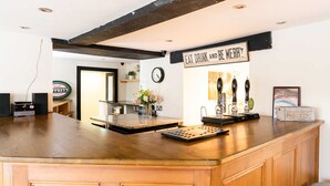 A bar area with a wooden counter, a clock, and a sign that reads "Eat Drink and Be Merry".