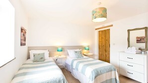 A bedroom with two beds, a wooden door, a white dresser, and a hanging lamp. - Superb barn conversion with games room, near Monyash, sleeps up to 20 in 7 bedrooms. (Monyash)