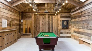A pool table with billiard balls, a dartboard, and a billiard cue rack in a wooden room with a sloped ceiling and exposed beams. - Superb barn conversion with games room, near Monyash, sleeps up to 20 in 7 bedrooms. (Monyash)