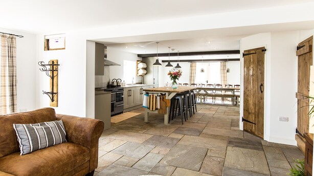 A spacious living area with a brown leather sofa, a kitchen with a central island, and a dining area with wooden tables and chairs. - Superb barn conversion with games room, near Monyash, sleeps up to 20 in 7 bedrooms. (Monyash)