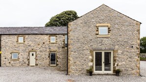 A stone building with a door and windows, gravel ground, and a tree in the background. - Superb barn conversion with games room, near Monyash, sleeps up to 20 in 7 bedrooms. (Monyash)