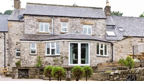 A stone building with a bay window, a small garden, and a stone wall with a wheel. - The Star in Taddington, 9 bedroom exclusive venue. Close to Buxton and Bakewell. (Buxton)
