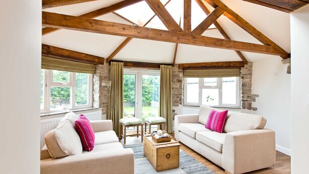 A cozy room with a vaulted ceiling, two sofas with cushions, a wooden coffee table, and a view of the outdoors through large windows. - The Star in Taddington, 9 bedroom exclusive venue. Close to Buxton and Bakewell. (Buxton)