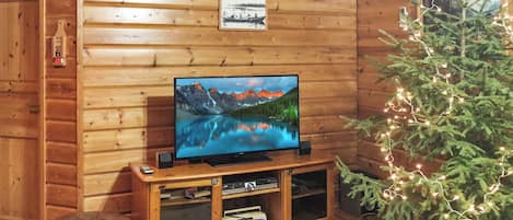 Ein Holzinterieur mit einem Fernseher auf einem Holzboden, einem kleinen, beleuchteten Weihnachtsbaum und einem gerahmten Bild an der Wand.