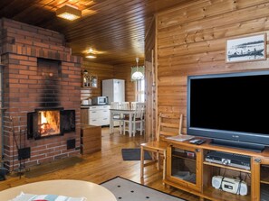 Interior acollidor d'una cabana amb una llar de pedra, parets de fusta, zona de menjador i un televisor.
