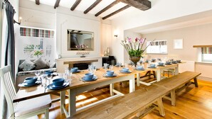 Un coin repas avec une longue table en bois dressée pour le repas, un canapé avec des coussins et un miroir au mur.