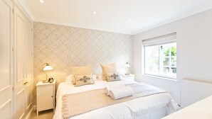 Une chambre à coucher avec un grand lit, deux tables de chevet avec des lampes, une fenêtre avec des stores et un papier peint à motifs floraux.