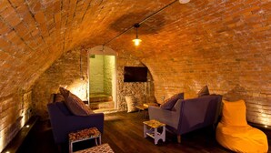 An attic room with brick walls, a television, two sofas, and a small table. - Victorian country house with 9 ensuite bedrooms, nestled in a pretty hamlet (Buxton)