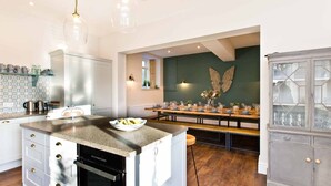 A modern kitchen with a central island, a dining area with a long table, and a decorative winged wall piece. - Victorian country house with 9 ensuite bedrooms, nestled in a pretty hamlet (Buxton)
