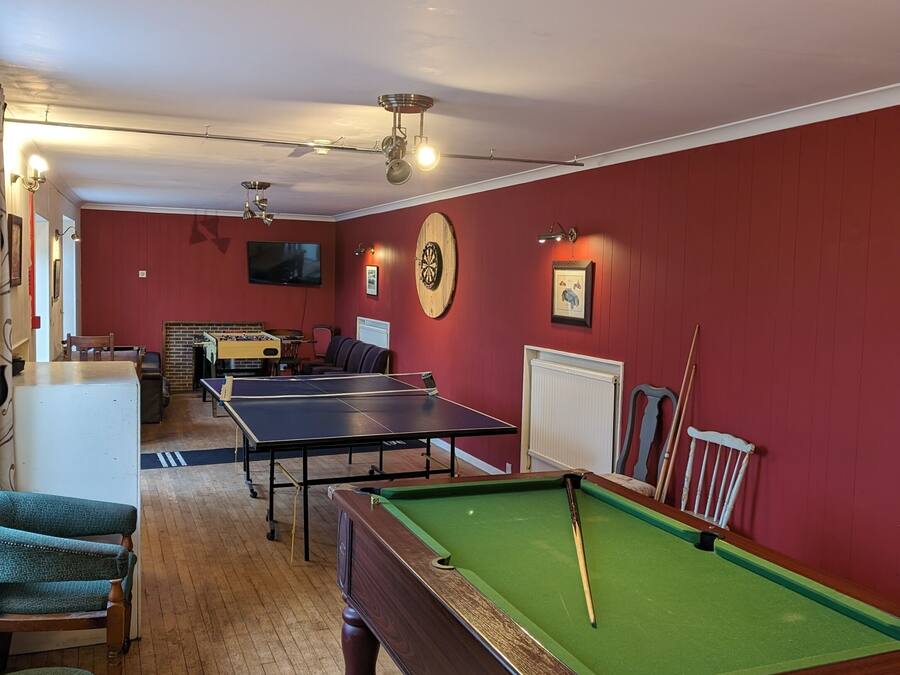 A billiards room with a pool table, two ping pong tables, and a dartboard.