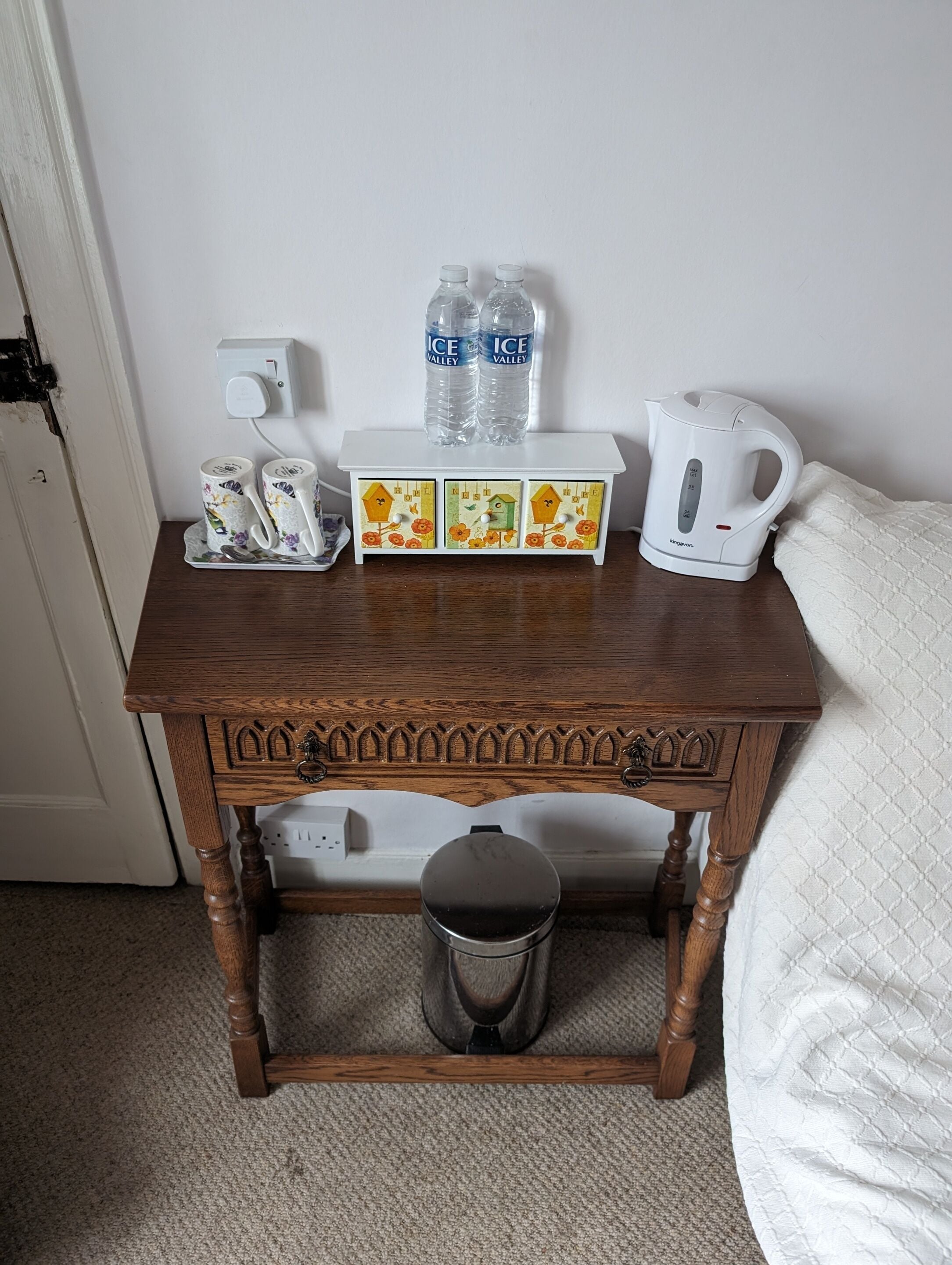 Una mesita de madera con una bandeja que contiene dos tazas, dos botellas de agua y una tetera eléctrica blanca.
