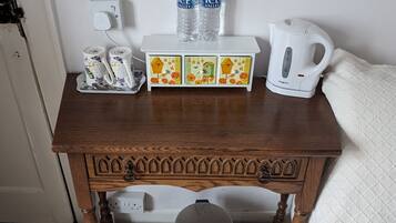 Una mesita de madera con una bandeja que contiene dos tazas, dos botellas de agua y una tetera eléctrica blanca.